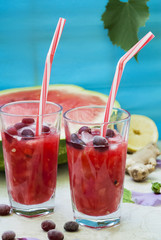 Watermelon cocktail with ginger, dogwood and lemon, decorated with flowers. In the background a watermelon on a blue background