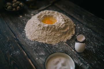 Food, cooking and baking concept. Baking bread in rustic kitchen. Dough recipe ingredients eggs, flour, milk, oil on dark vintage wooden table from above. Rural kitchen. Homemade food.