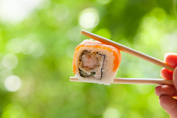 hand holding chopsticks sushi roll with red fish on summer natural background