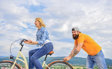 Woman rides bicycle sky background. Push and promoting. Impulse to move. Man pushes girl ride bike. Support helps believe in yourself. Feel impulse to start moving. Girl cycling while man support her