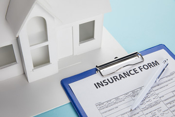 close-up view of insurance form and small house model with clipboard and pen on blue