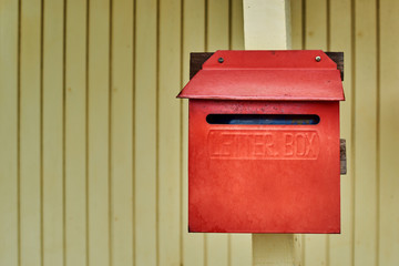 Old red mailbox on light yellow wooden wall  background.