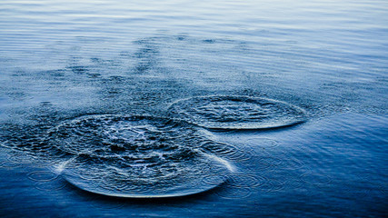 Round droplets of water over the circles on the water. Water drop, whirl and splash. Ripples on sea...