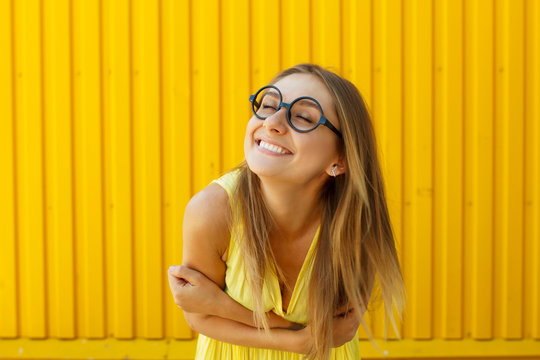 Beautiful young woman in funny toy glasses smiling over yellow background at daylight