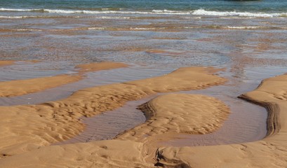 Grooves and inlets in sand on beach with waves in background