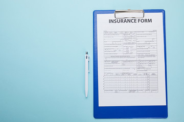 top view of insurance form on clipboard and pen isolated on blue