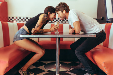 Romantic couple sharing a glass of milk shake at a restaurant - obrazy, fototapety, plakaty