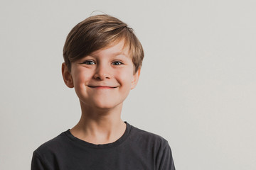 a portrait of cute boy pulling faces, dark grey shirt, white wall