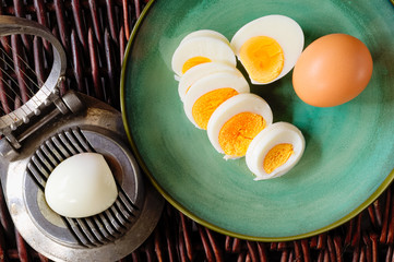 Hard-boiled egg cut and piled on egg slicer and full egg with shell on green plate or dish.