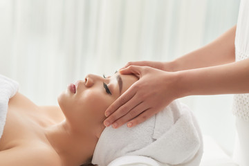 Crop hands of massage therapist rubbing carefully forehead of beautiful lady during spa session in salon