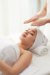 Fototapeta na wymiar Crop massage therapist holding hands over face of attractive woman during spa session in nice salon