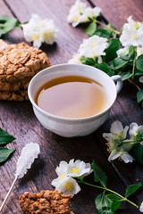 Tea with jasmine and oatmeal cookies on a brown wooden background, white flowers around