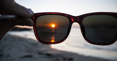 Sunglasses framing a beautiful beach sunset on a cloudless day.