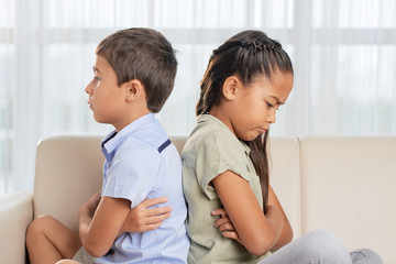 Side view of Asian brother and sister sitting on comfortable sofa in living room after quarrel