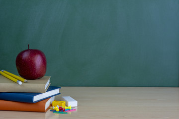 Libros y materiales escolares para la vuelta al colegio  en la mesa de la clase frente a la pizarra verde 