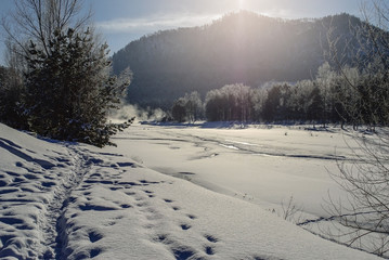 Fototapeta na wymiar Winter landscape. Trees covered with snow, frozen river, path in snowdrift and silhouette of hill