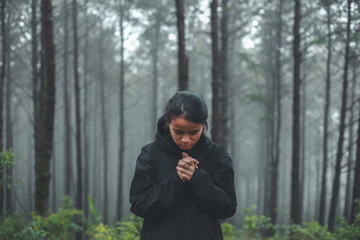 The woman is praying to God in the forest.