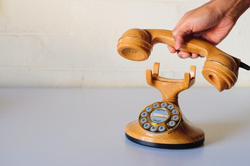 Hand and old style in plastic like wood and golden dial phone pretending to make a call or hang up