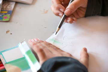 Creative workshop for kids. Little boy drawing on white paper at school. Glue, colorful pencils and star shaped paper cutter on table. Making decorations. Concept of art, crafts and kids having fun