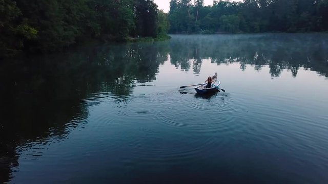 aerial view of young readhead female traveler in the boat on the lake with two siberian husky dogs