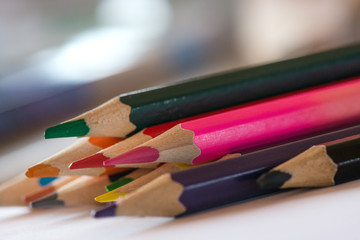 Fototapeta premium Pile of sharp coloured drawing pencils on table. Rainbow colors red, yellow, blue, green, purple. Concept of art, crafts and kids having fun 