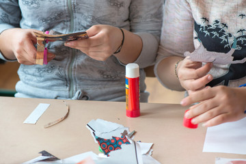 Creative workshop for kids. Little girls gluing cut out shapes and characters from magazines on white paper. Concept of art, crafts, kids having fun. Making collages and creating stories. Messy desk