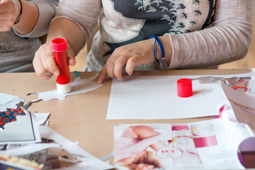 Creative workshop for kids. Little girls gluing cut out shapes and characters from magazines on white paper. Concept of art, crafts, kids having fun. Making collages and creating stories. Messy desk