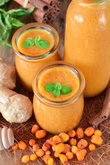Yellow smoothie with berries of sea buckthorn in glass jars topped with mint