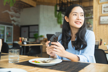 Beautiful young woman using an application to send an sms message in her smartphone at restaurant.