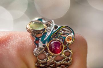 Macro shot of silver engagement ring on colorful, sparkling background. Wedding ring with prehnite stone, ruby and sapphire crystals. Royal, expensive and luxury gift