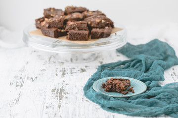 Homemade Brownie with Pecans Isolated on Teal Plate with Cake Plate full of Brownies in the Background; White Background; White Rustic Table
