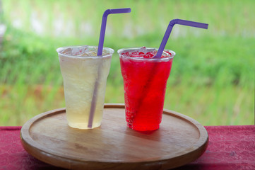 Sweet juice in plastic glass Place on round wooden tray with blurred soft of green rice paddies.