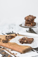 Homemade Brownie with Pecans on Parchment Paper; Brownies Stacked on Pedestal in Background; Black & White Kitchen Towel