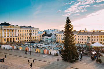 Fototapeta premium Helsinki, Finland. People Walking On Christmas Xmas Market With Christmas Tree On Senate Square In Background Of Government Palace At Winter Sunny Day.