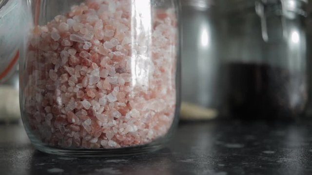 Close up of Himalayan rose pink salt pouring into Kilner clip top jar in kitchen.