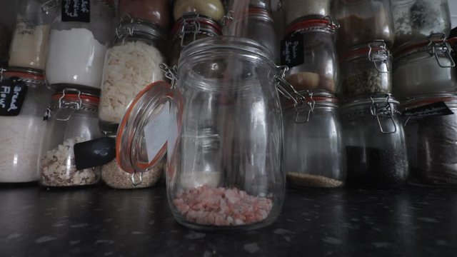 Himalayan rose pink salt pouring into Kilner clip top jar infant of wall of ingredients.