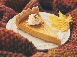 Piece of pumpkin cake with cream and nuts on plate on cosy knitted throw.