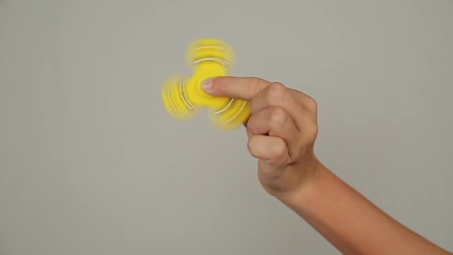 someones hand showing trick with two fidget spinners on light gray background, popular relaxing toy, generic design.