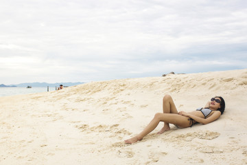 Fototapeta na wymiar Young Asian woman in bikini laying on sandy beach, sexy woman enjoy at the beach