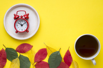 Abstraction, the concept of autumn. Autumn leaves, clock alarm clock and Cup of coffee on yellow background.