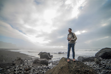 Fototapeta premium Man traveler stood on the rock to enjoy the view at Black sand beach, Vik. Iceland