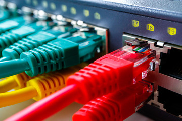 red cables in the foreground inserted in the switch ports in the background green and yellow patchcords