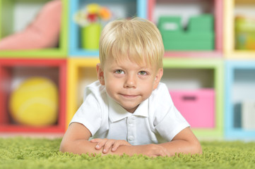 Portrait of blonde little boy lying on green carpet 