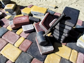 A pile of colored bricks of the tiles 'Old Town' and a rubber hammer for laying paving slabs. Beautiful yellow, red and black rectangular blocks, bright wallpaper or background on the building theme