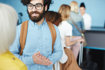 Cheerful bearded man standing and interacting with blonde woman in queue to check in