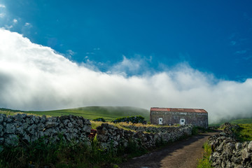 A house on a green mountain with some clouds and blue Sky in Corvo Island Azores