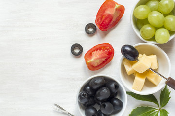 Ingredients for snacks, cheese with olives and tomato, grape on a white table with copy space.