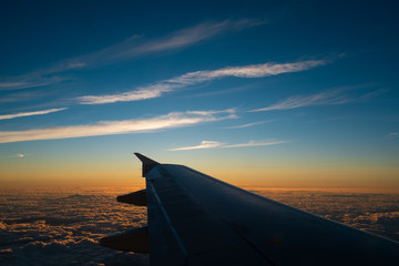 Sunset trough the window of an air plane and a wing with some clouds