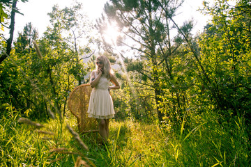 Caucasian Woman in forest alone in white dress with wicker chair
