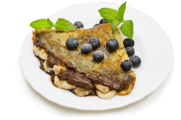 Homemade crepes served with fresh blueberries and powdered sugar on rustic wooden table in cast iron skillet